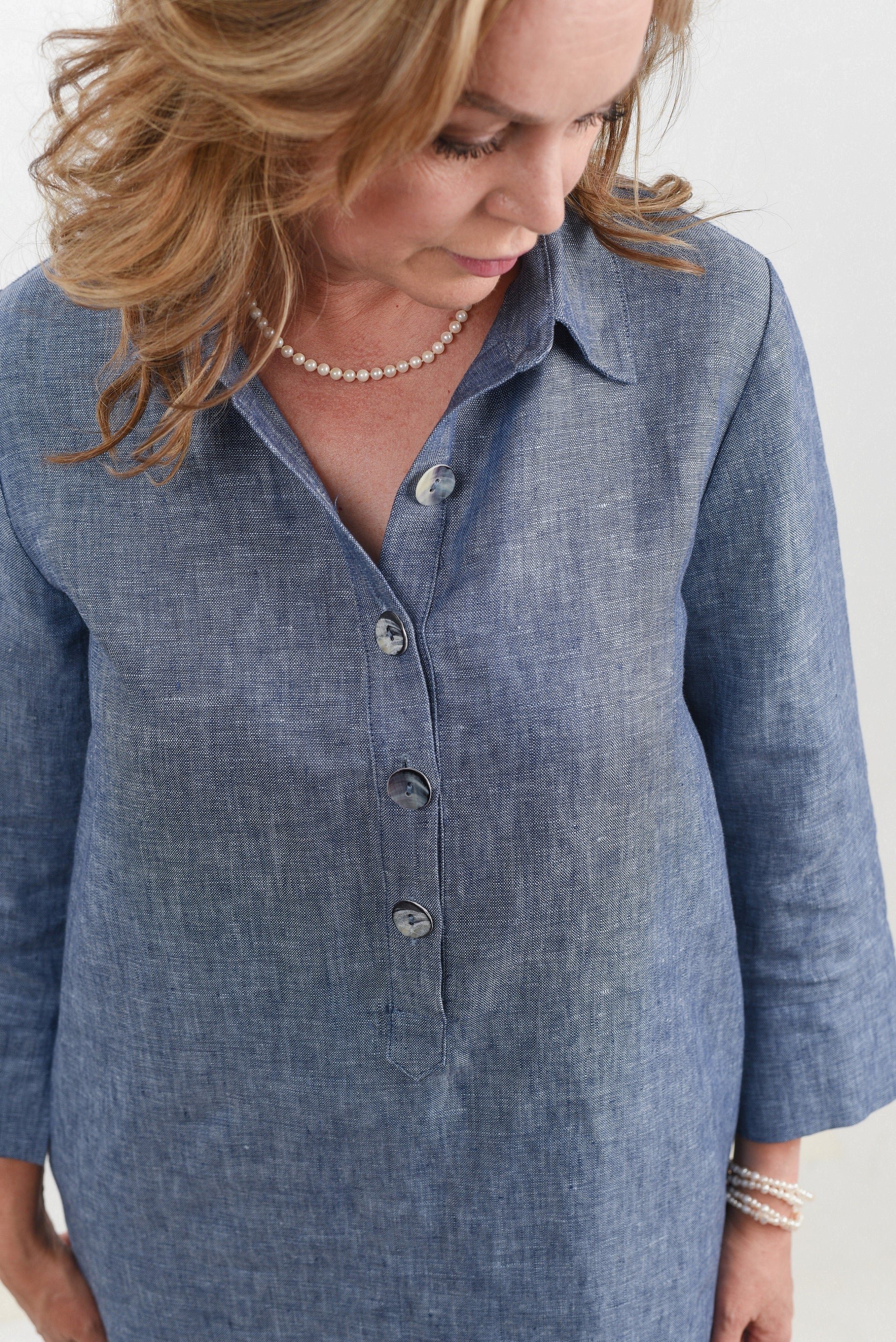 Close-up of a woman in a blue linen dress with pearl accessories